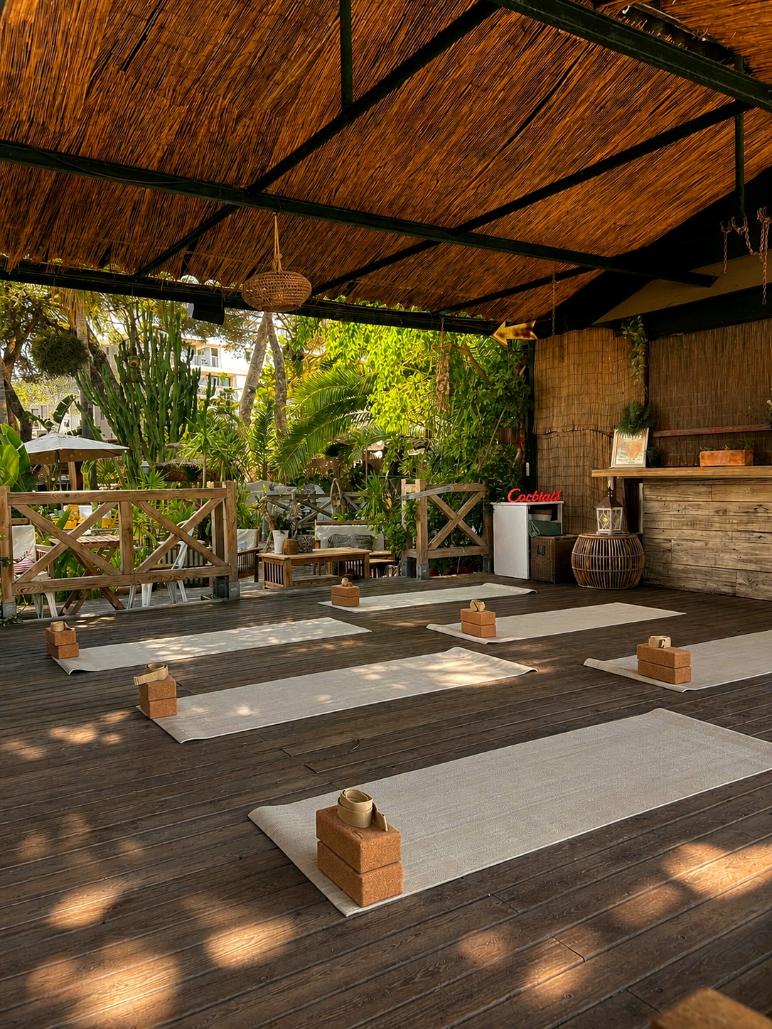 Yoga mats laid out under the palm-thatch roof at Kalima Beach, surrounded by tropical plants